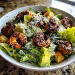 A close-up of a delicious Blackened Shrimp Caesar Salad topped with grated Parmesan cheese and croutons in a white bowl.