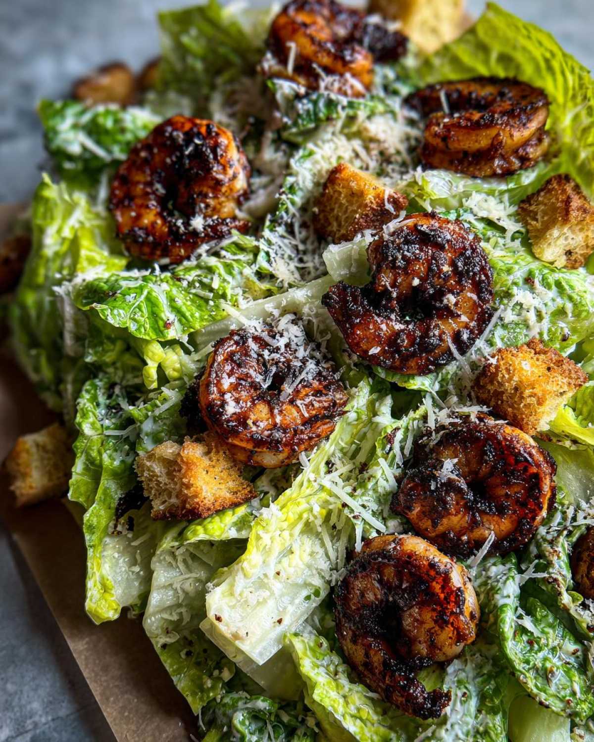 Close-up view of a vibrant Blackened Shrimp Caesar Salad topped with dark, seasoned shrimp, grated Parmesan, and golden croutons.
