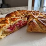 A slice cut from a golden, flaky Blood Orange and Rhubarb Geometric Galette showing the bright pink rhubarb filling.
