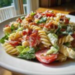 Close-up of a creamy BLT Pasta Salad featuring rotini pasta, crisp lettuce, halved cherry tomatoes, and crumbled bacon.