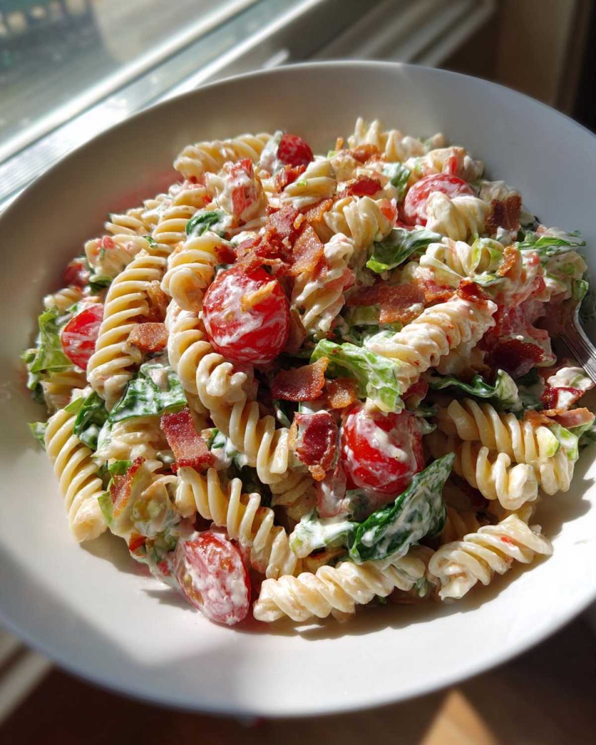 A close-up of a bowl of creamy BLT Pasta Salad featuring rotini pasta, cherry tomatoes, lettuce, and crispy bacon pieces.