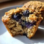 A close-up of a high-protein cottage cheese muffin, broken open to show moist interior and whole blueberries.