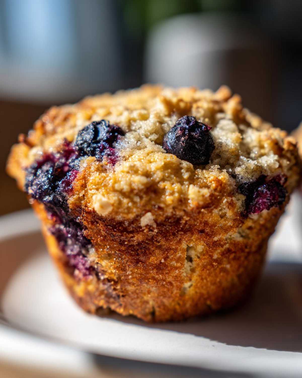 A close-up shot of a golden brown, crumb-topped blueberry cottage cheese muffins sitting on a white plate.
