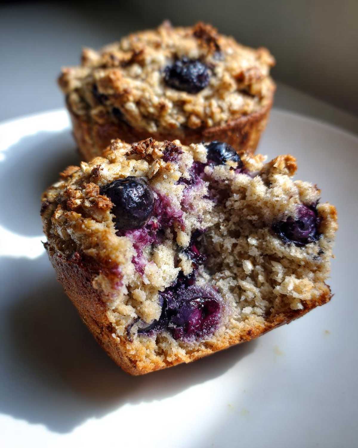 A blueberry cottage cheese muffin cut in half showing the moist, oat-topped interior packed with blueberries.
