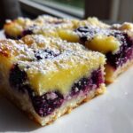 Close-up of two decadent Blueberry Lemon Pie Bars dusted with powdered sugar on a white plate.