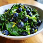 Close-up of a vibrant Blueberry Pistachio Spring Salad featuring dark green leaves, fresh blueberries, and chopped pistachios in a white bowl.
