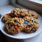 A plate of chewy oatmeal Monster Cookies loaded with chocolate chips and colorful M&M candies.