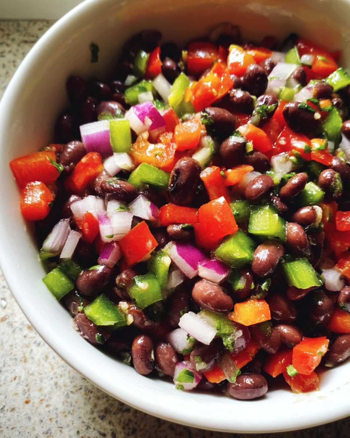 Close-up of vibrant Texas Caviar featuring black beans, red onion, green peppers, and tomatoes in a white bowl.