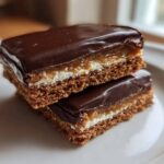 Two stacked bars of buckeye graham crackers showing a chocolate topping, caramel, cream layer, and graham cracker base.