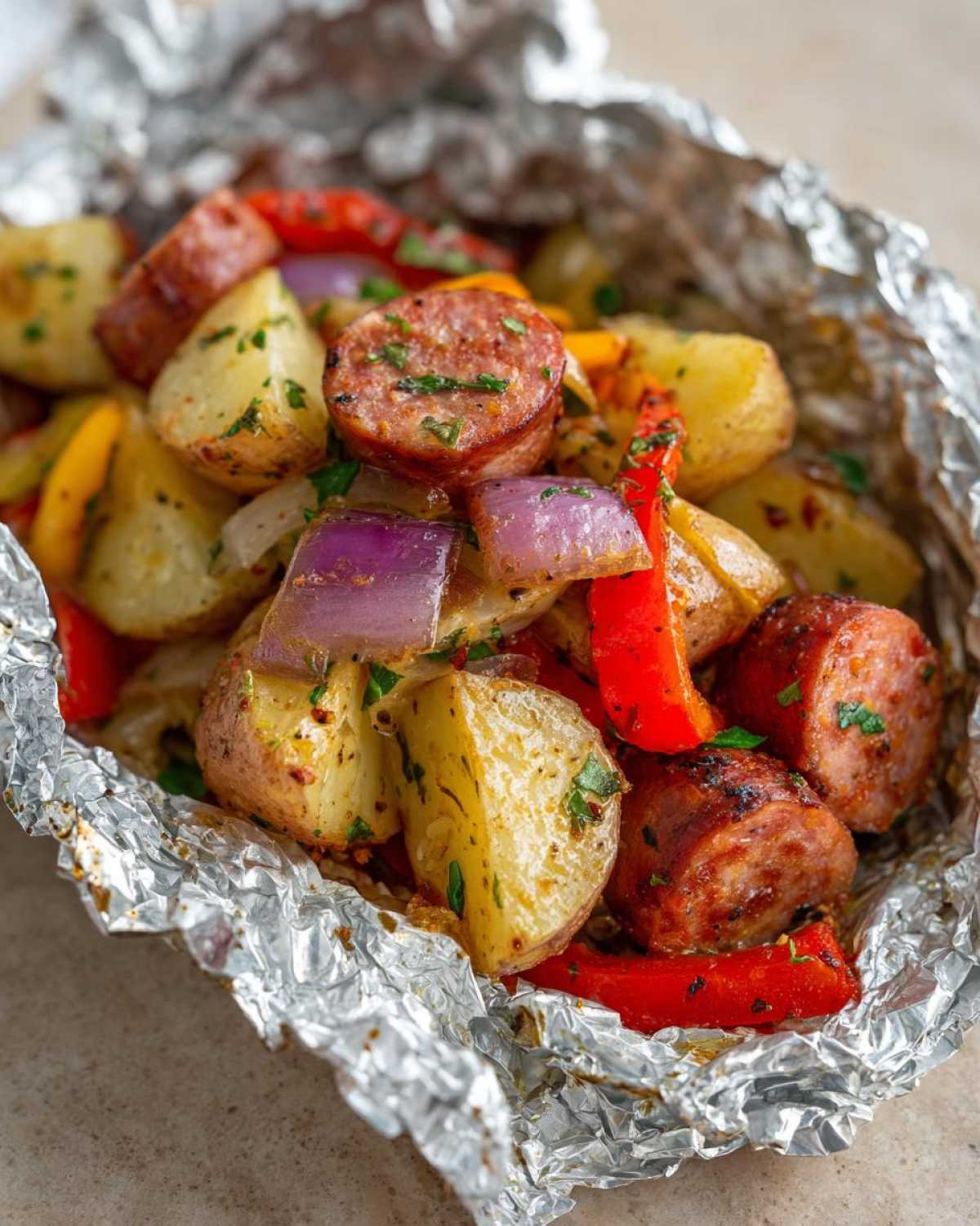 Close-up of seasoned Campfire Potatoes mixed with sliced sausage, red peppers, and purple onions cooked in a foil packet.