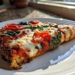 Close-up of a thick slice of Cauliflower Crust Margherita Pizza topped with mozzarella, tomatoes, and spinach.