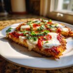 Two slices of golden Cauliflower Crust Margherita Pizza topped with melted mozzarella, red sauce, and fresh basil.