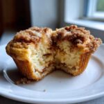 A close-up of Cheesecake Muffins with Cinnamon cut in half, showing the creamy filling and crumb topping.