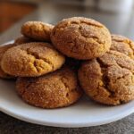 A stack of chewy pumpkin snickerdoodles coated in cinnamon sugar resting on a white plate.