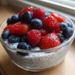 A close-up of Chia Seed Pudding with Fresh Berries, topped with vibrant strawberries, raspberries, and blueberries, served in a glass bowl.