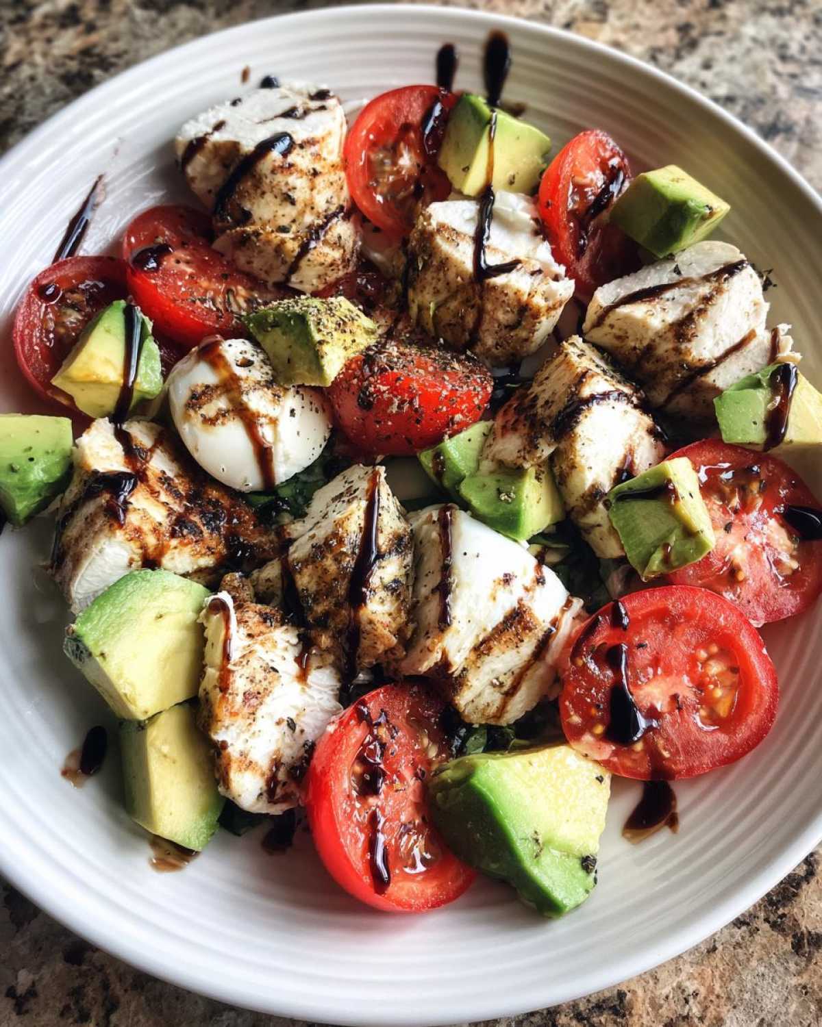 Close-up of a vibrant Chicken Avocado Caprese Salad featuring grilled chicken, mozzarella, tomatoes, and avocado chunks drizzled with balsamic glaze.