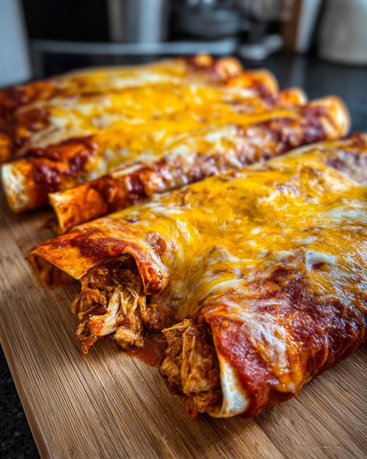 Close-up of four baked chicken Enchiladas covered in red sauce and melted yellow cheese, showing shredded chicken filling.