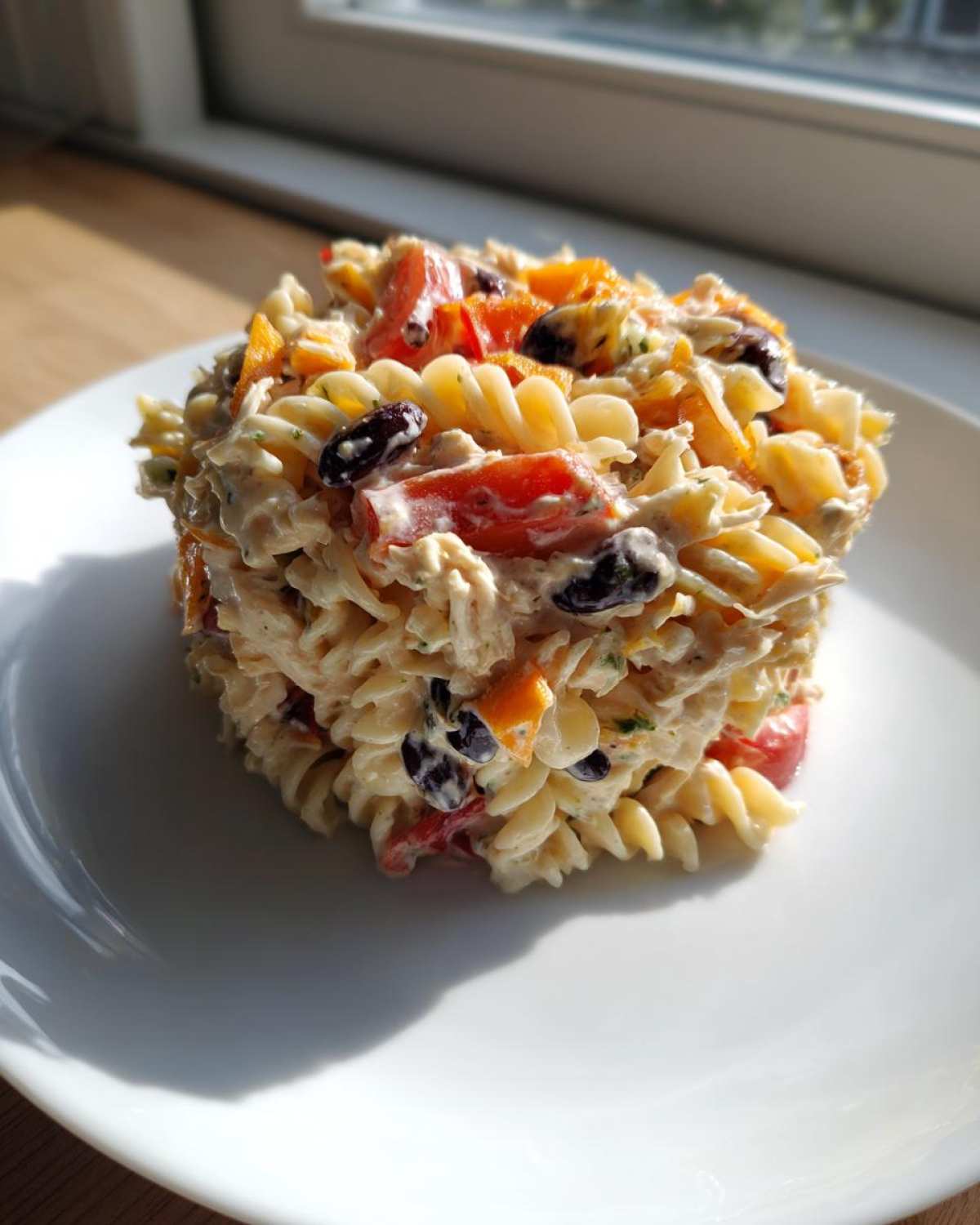 A molded serving of creamy Chicken Taco Pasta Salad featuring rotini pasta, black olives, and red peppers, sitting on a white plate.