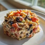 A molded serving of creamy Chicken Taco Pasta Salad with black beans, tomatoes, and shredded cheese.