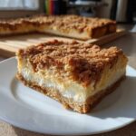 A close-up of a rich slice of churro cheesecake bars featuring a thick, creamy filling and a cinnamon-sugar crumb topping.