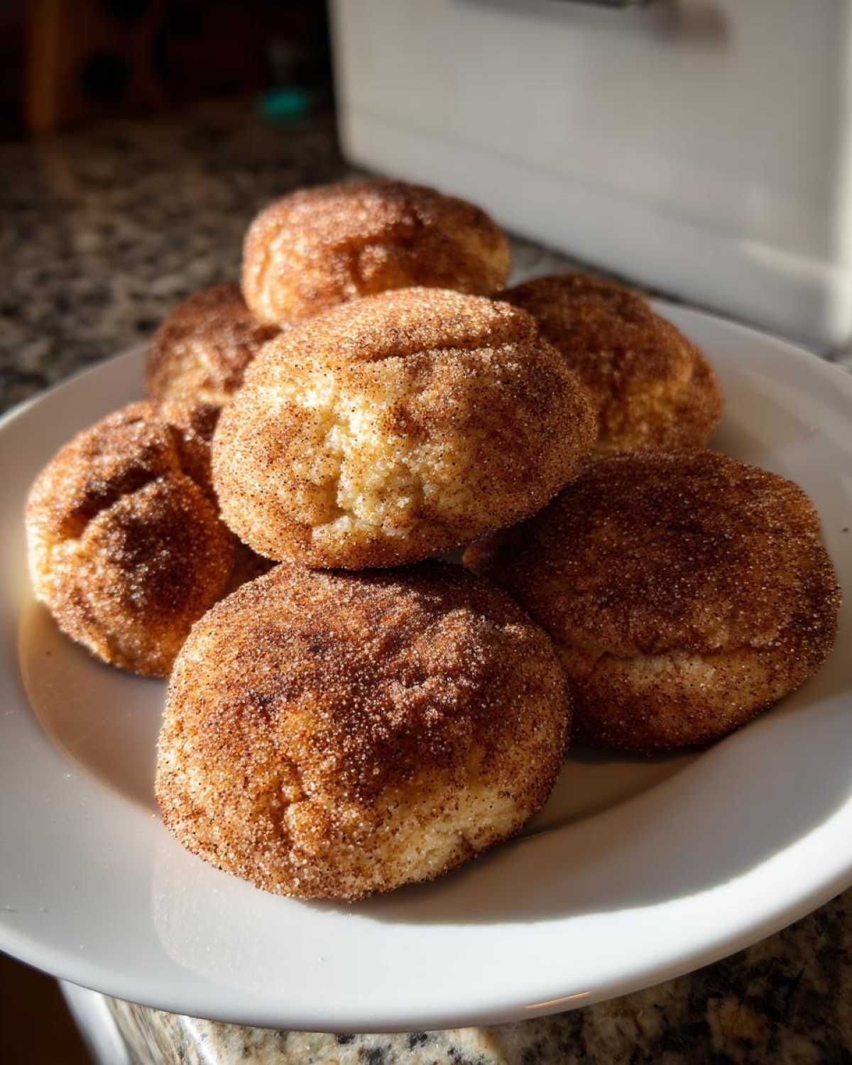 A stack of soft, round churro cookies generously coated in cinnamon sugar resting on a white plate.