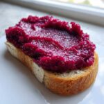 Close-up of thick, vibrant magenta Cinnamon Rhubarb Butter spread generously over a slice of toasted bread.