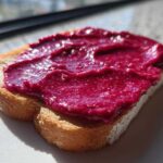 Close-up of toast generously spread with vibrant, deep magenta Cinnamon Rhubarb Butter, glistening in the sunlight.