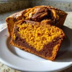 A thick slice of vibrant orange Cinnamon Swirl Pumpkin Bread showing a rich chocolate swirl pattern, resting against the loaf.