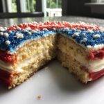 Cross section view of the Classic Buttermilk Flag Cake showing layers of yellow cake and white frosting, decorated with red, white, and blue sprinkles.