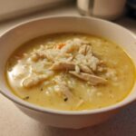 Close-up of a white bowl filled with Classic Greek Lemon Chicken Soup featuring shredded chicken and rice in a creamy yellow broth.