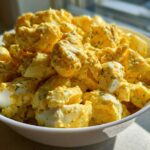 A white bowl filled with creamy Classic Mustard Potato Salad featuring chunks of potatoes and visible pieces of hard-boiled egg.