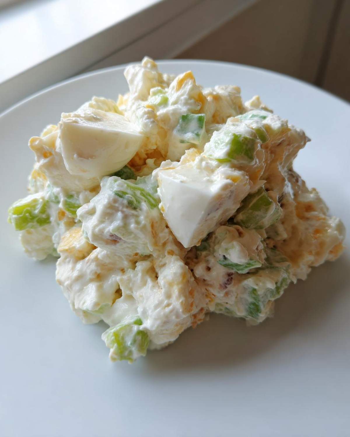 A scoop of creamy Classic Potato Salad featuring chunks of potato, hard-boiled egg, and green celery, served on a white plate.
