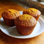 Three moist, golden-brown Classic pumpkin muffins sitting on a white plate.