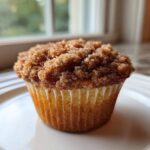 A single, perfectly baked Coffee Cake Muffins featuring a thick, sugary cinnamon crumb topping, resting on a white plate.
