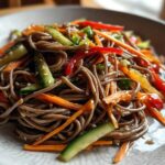 Close-up of a serving of Cold Soba Noodle Salad with ginger soy dressing, mixed with julienned carrots, cucumbers, and red peppers.