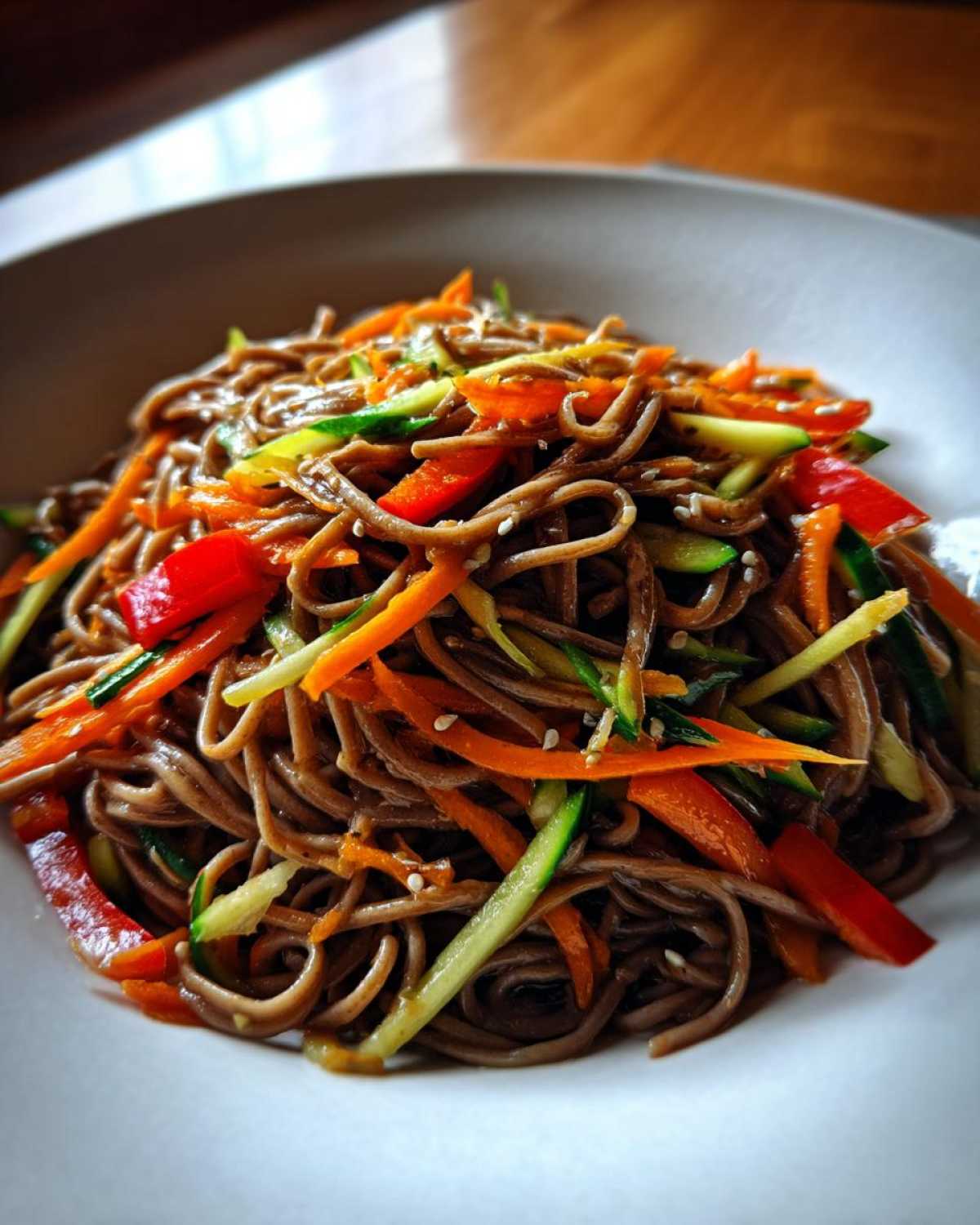Close-up of Cold Soba Noodle Salad tossed with julienned carrots, cucumbers, and red peppers, sprinkled with sesame seeds.