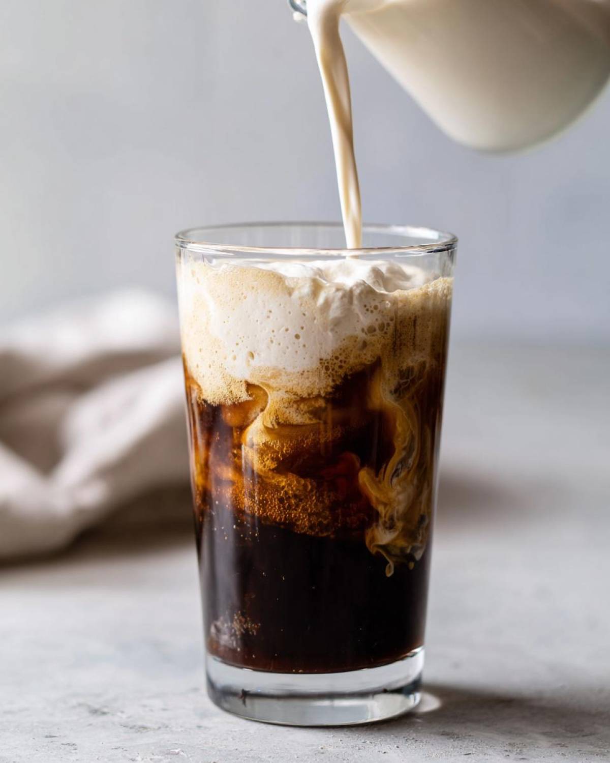 Pouring thick, creamy foam onto cold brew coffee to make Copycat Starbucks Vanilla Sweet Cream Cold Foam.