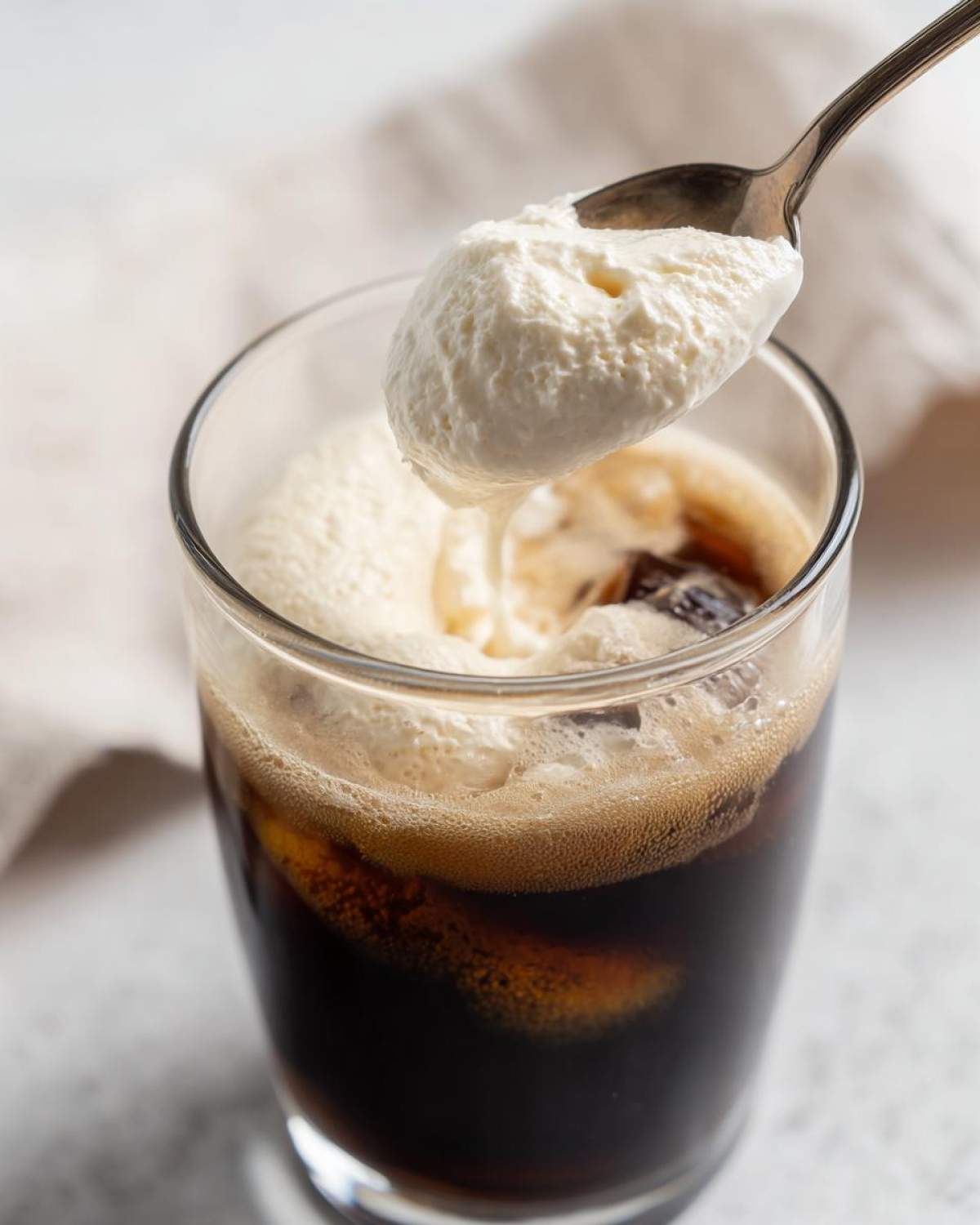 A spoon loaded with thick Copycat Starbucks Vanilla Sweet Cream Cold Foam being added to iced coffee.