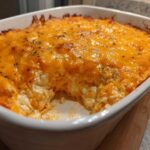 Close-up of baked cottage cheese buffalo chicken dip in a white casserole dish with a scoop removed.