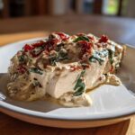A single serving of Cream Cheese Chicken Bake topped with a creamy sauce, spinach, and sun-dried tomatoes on a white plate.