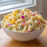 A large white bowl overflowing with creamy Amish macaroni salad featuring elbow pasta and colorful diced vegetables.