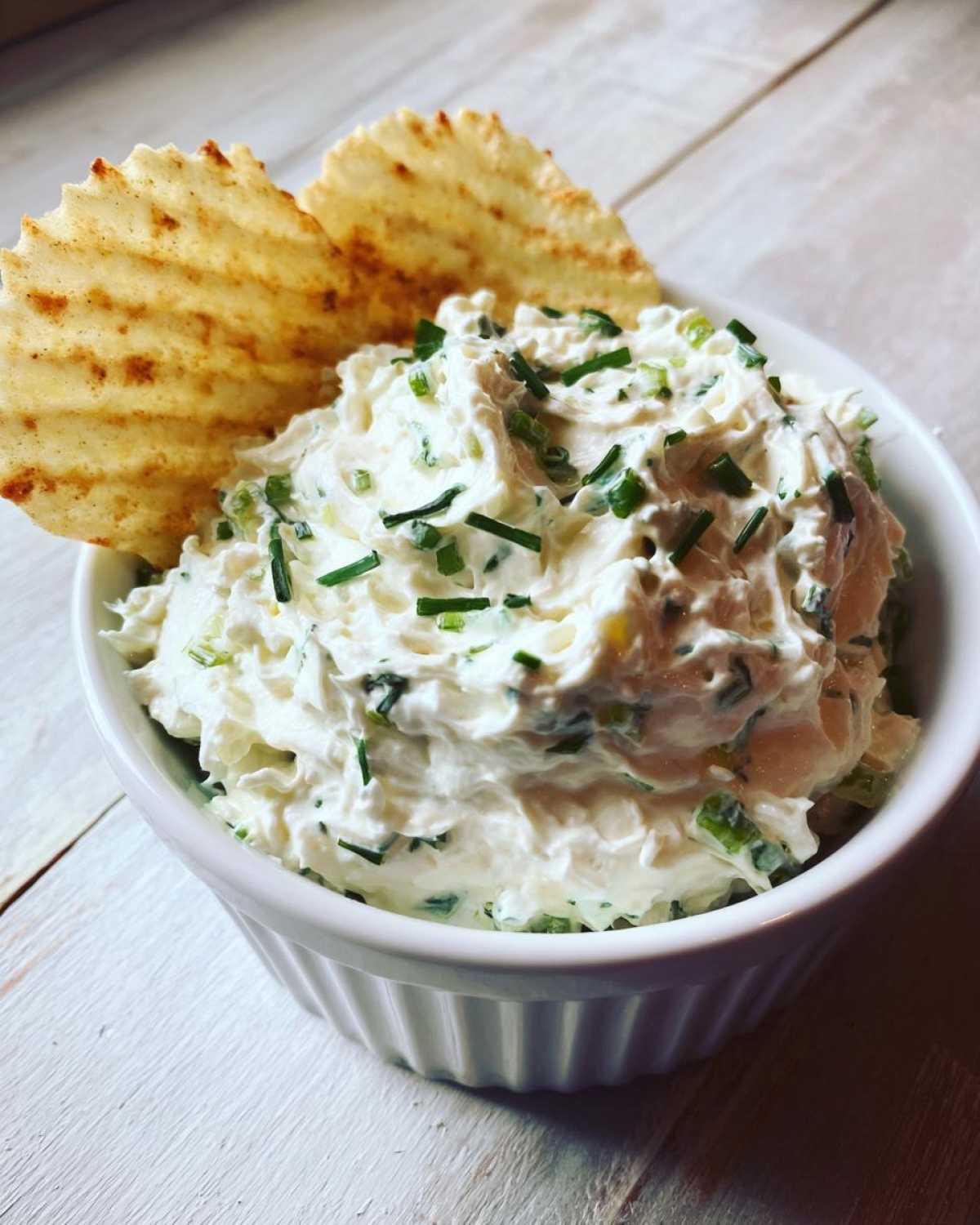 Close-up of creamy Boat Dip topped with chives, served with two ruffled potato chips.