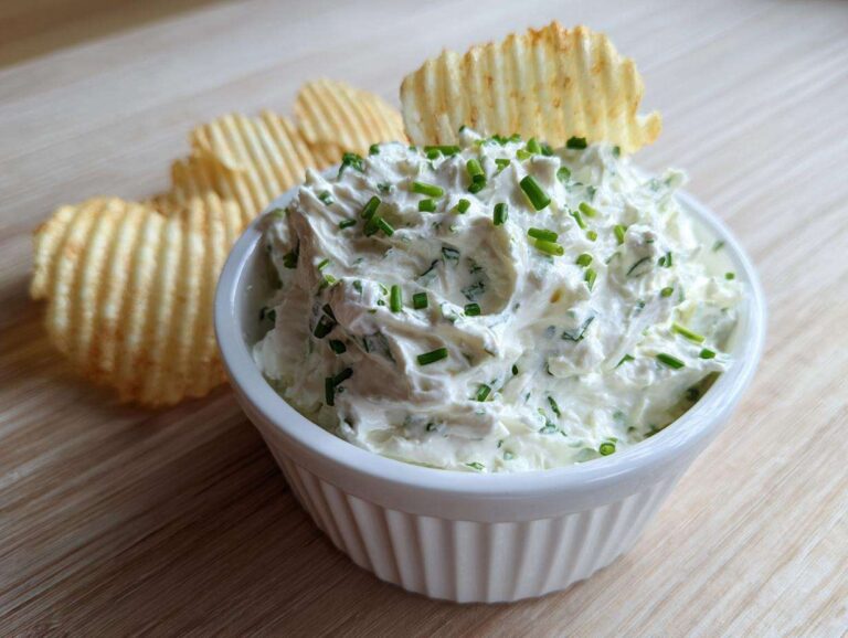 A white bowl filled with creamy Boat Dip topped with fresh chives, served with ruffled potato chips.