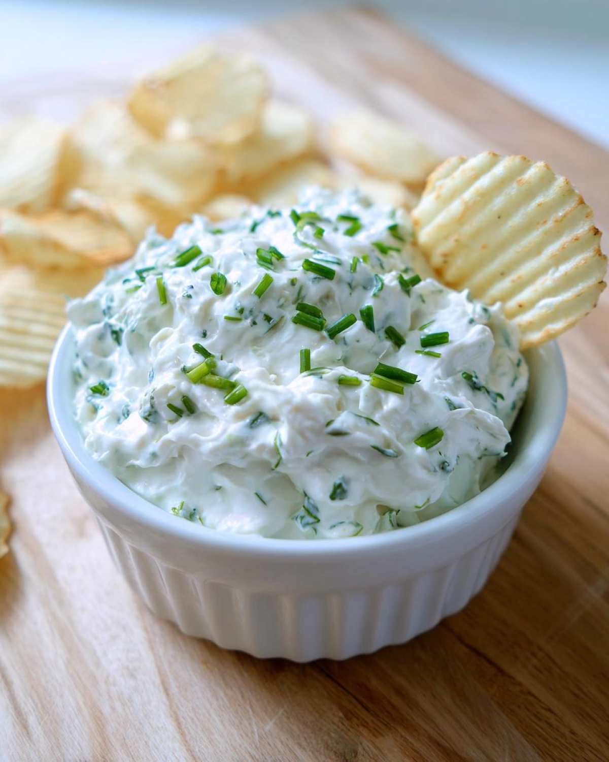 A white bowl filled with creamy Boat Dip topped with fresh chives, served with ruffled potato chips.