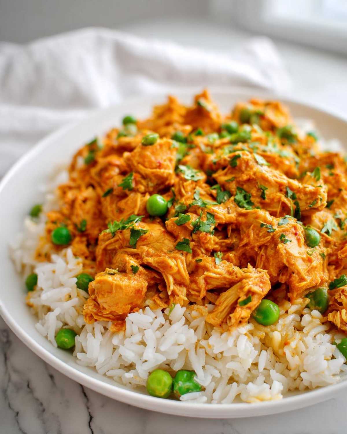 Close-up of shredded, saucy Cajun chicken served over white rice with green peas and fresh cilantro garnish.