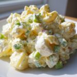 A mound of creamy Classic Potato Salad featuring chunks of potato and green celery, served on a white plate.