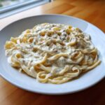 A close-up of fettuccine pasta coated in creamy cottage cheese alfredo sauce and topped with cracked black pepper.