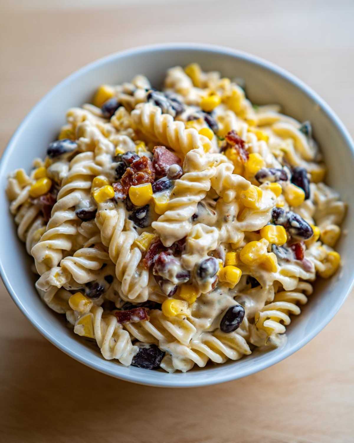 Close-up of creamy Cowboy Pasta Salad featuring rotini pasta, black beans, corn, and bits of sun-dried tomato or bacon.