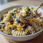 A spoonful of creamy Cowboy Pasta Salad featuring rotini pasta, corn, black beans, and bacon being lifted from a white bowl.