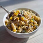 A spoonful of creamy Cowboy Pasta Salad featuring rotini pasta, black beans, and corn being lifted from a white bowl.
